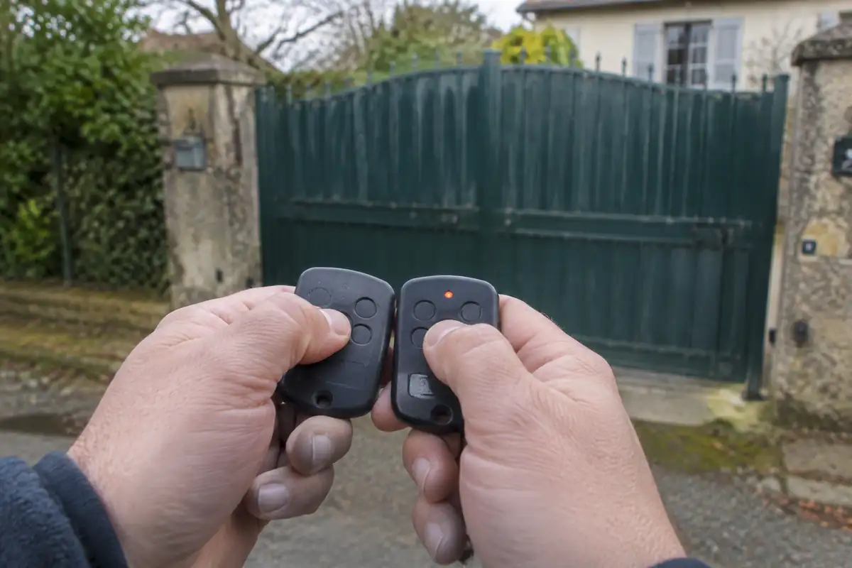 Deux télécommandes de portail tenues bout à bout devant un portail, un voyant allumé pendant la copie