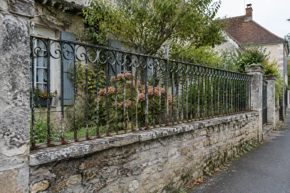 Grille ancienne en fer forgé posée sur un muret de pierre le long d'une rue de village
