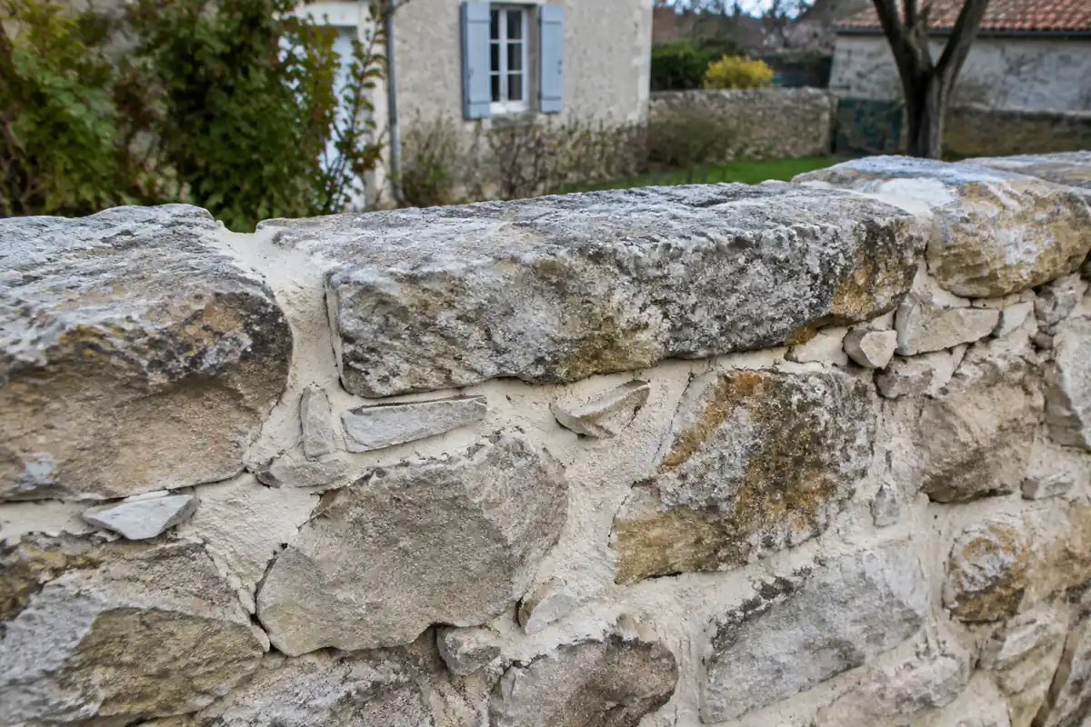 Haut d'un muret en moellons en cours de montage, une pierre posée en travers lie les deux faces dans le mortier de chaux