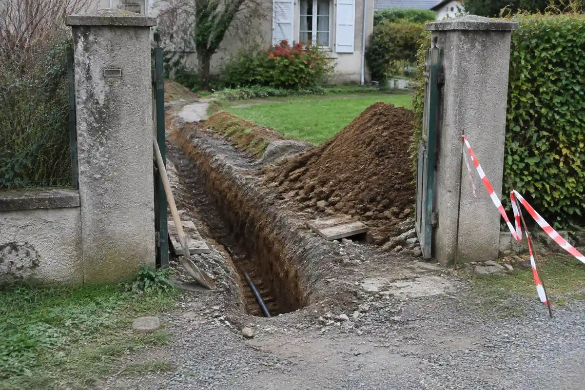 Tranchée creusée devant deux piliers en béton à l'entrée d'un jardin